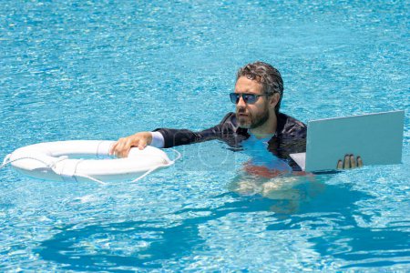 Téléchargez les photos : Secours. Un homme d'affaires en costume tient un ordinateur portable et une bouée de sauvetage dans une piscine. Bague de sauvetage pour homme d'affaires. Sauvetage homme d'affaires. Enregistrer et aider les entreprises - en image libre de droit