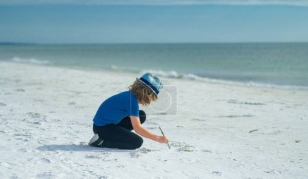 Téléchargez les photos : Face d'enfant d'été. Enfant mignon dessiner un sur le sable profiter de la mer d'été et de rêver. Petit garçon drôle jouer sur la plage d'été. Happy boy bénéficie de la vie sur la plage d'été - en image libre de droit