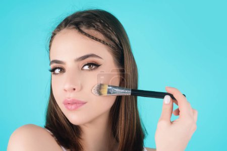 Téléchargez les photos : Woman applying foundation powder or blush with makeup brush. Facial treatment, perfect skin, natural make up, facial beauty. Isolated on studio background. Applying makeup - en image libre de droit