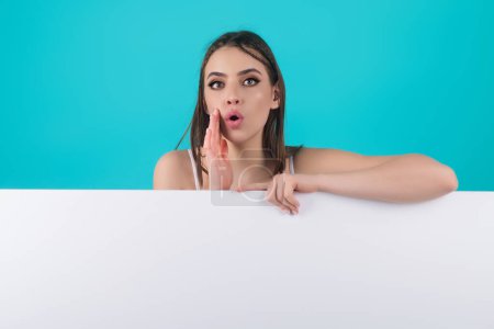 Photo for Woman holding a blank billboard isolated on studio background. Cheerful cute girl is standing behind the white blank banner, copy space. Empty blank board. Studio female portrait with empty board - Royalty Free Image
