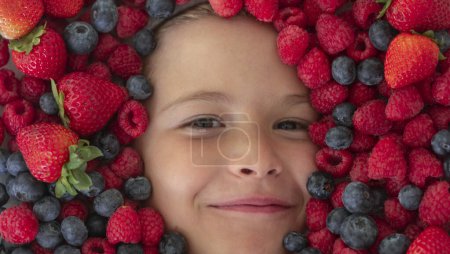 Photo for Mix of berries. Kids face with fresh berries fruits. Assorted mix of berries strawberry, blueberry, raspberry, blackberry on background. Healthy nutrition berries for kids - Royalty Free Image