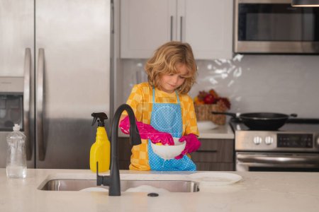 Foto de Niño lavando los platos en el fregadero de la cocina. Detergentes y accesorios de limpieza. Servicio de limpieza. Pequeño niño limpieza - Imagen libre de derechos