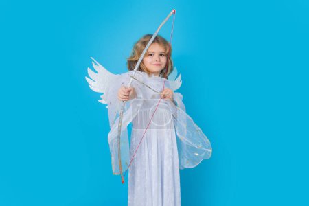 Photo for Angel kid shoots a love arrow from a bow on Valentines Day. Valentines day. Kid with angel wings. Studio portrait of angel child on studio color isolated background with copy space - Royalty Free Image