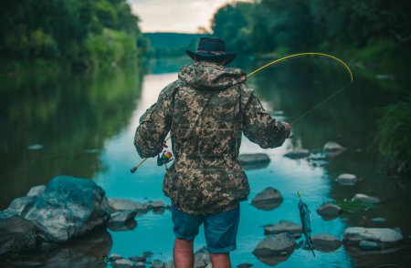 Foto de Back view of man with fishing rod, fisherman men in river water outdoor. Summer fishing hobby - Imagen libre de derechos