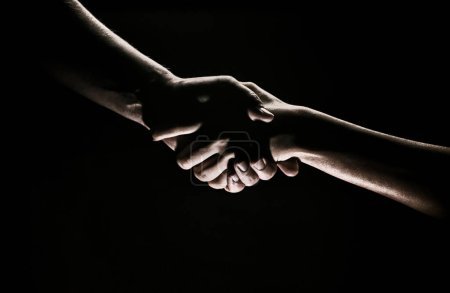 Téléchargez les photos : Handshake hand, arm on salvation. Close up help hand. Two hands, helping arm of a friend, teamwork. Rescue, helping gesture or hands, agreement. Black background - en image libre de droit