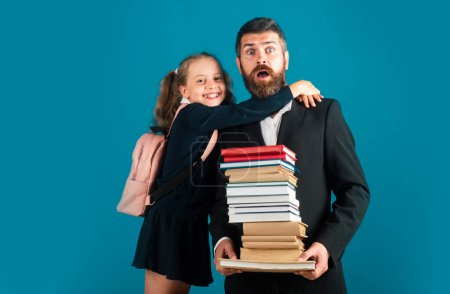Photo for Elementary pupil hugging teacher in studio. Funny father or teacher with school girl daughter hold big stack school textbook notebook books, isolated on blue - Royalty Free Image