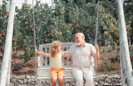 Foto de Abuelo e hijo balanceándose en el jardín. Abuelo y nieto jugando en swing. Generaciones edades - Imagen libre de derechos