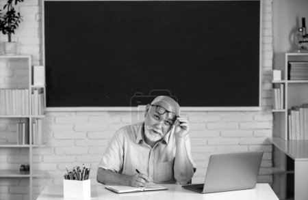Photo for Portrait of senior teacher teaching line of high school students with notebook in classroom on blackboard. Aged male retired teacher - Royalty Free Image