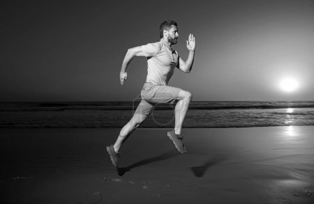 Photo for Man running at sunset. Full length of healthy man running and sprinting outdoors. Male runner. Fit man fitness model working outdoor by sea beach. Run on sea sandy beach. Sport sprint - Royalty Free Image