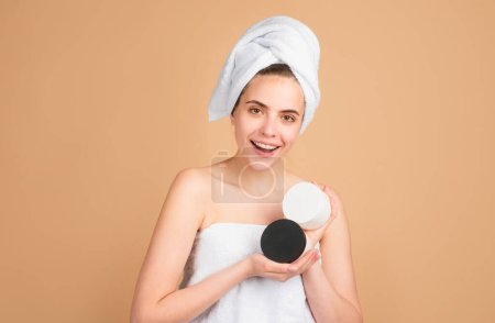 Photo for Beautiful happy girl with cream bottle, clean fresh skin. Facial treatment. Cosmetology beauty and spa. Girl apply skincare cream on face. Gestures for advertisement. Beige background. - Royalty Free Image