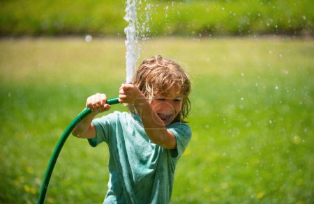 Photo for Little gardener child helping to watering flowers with garden hose in summer garden. Seasonal yard work - Royalty Free Image