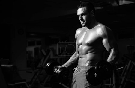 Foto de Sport man man doing biceps lifting in a gym. Young muscular man with naked torso working out in gym. Athletic male sport man exercising. Fitness sports concept - Imagen libre de derechos