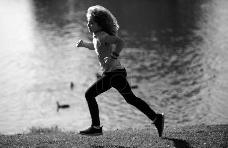 Foto de Niños corriendo al aire libre. Carrera y deporte saludable para los niños. Niño corriendo en el campo de verano cerca del lago, los niños fitness. Ejecutando entrenamiento. Deportes al aire libre y fitness para niños, ejercicio al aire libre - Imagen libre de derechos