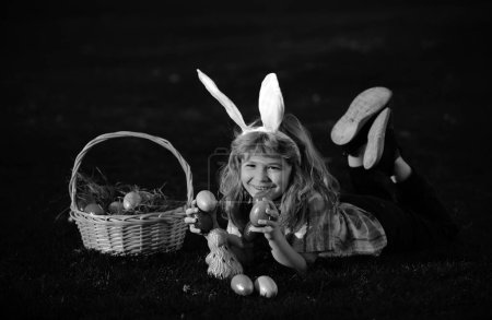 Photo for Children hunting easter eggs. Kid boy lying on the grass and finding egg. Child with easter eggs and bunny ears, outdoor portrait. Child bunny boy with rabbit bunny ears - Royalty Free Image