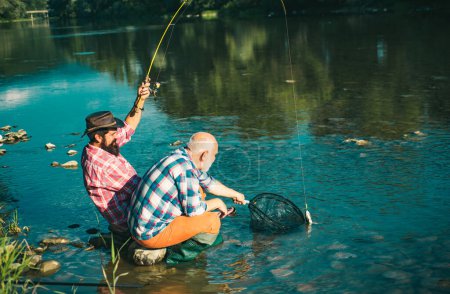 Téléchargez les photos : Deux hommes amis pêche. Pêcheur à la ligne fait coulée, debout dans l'eau de la rivière. Vieux et jeune pêcheur. Pêcher la truite - en image libre de droit