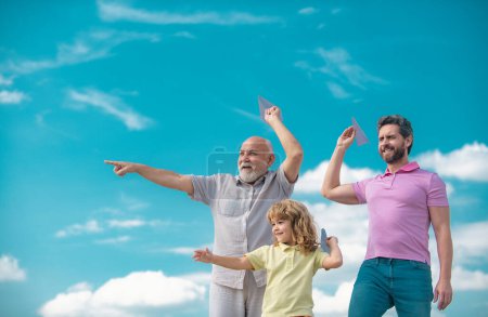 Téléchargez les photos : Génération hommes : grand-père père et petit-fils jouant avec jouet avion en plein air sur le ciel. Garçon rêve de devenir pilote - en image libre de droit
