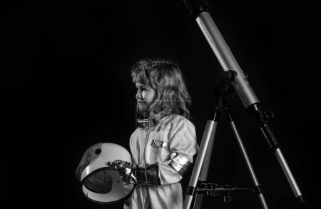 Foto de Niño jugando a ser astronauta con casco espacial, traje de metal y telescopio. Éxito, creatividad y concepto de puesta en marcha - Imagen libre de derechos
