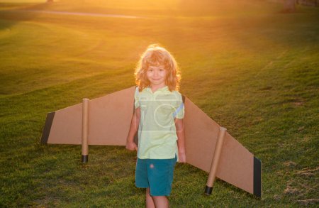 Photo for Kid pilot with backpack wings at sunset grass field. Child playing pilot aviator and dreams outdoors in park - Royalty Free Image