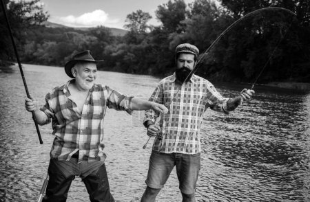 Téléchargez les photos : Père et fils mature pêcheur pêche avec une canne à pêche sur la rivière. Pêcher la truite - en image libre de droit
