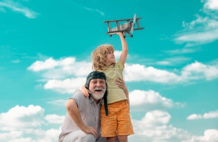 Téléchargez les photos : Petit-fils enfant et grand-père avec jetpack jouet avion contre ciel. Enfant pilote aviateur avec des rêves d'avion de voyager - en image libre de droit