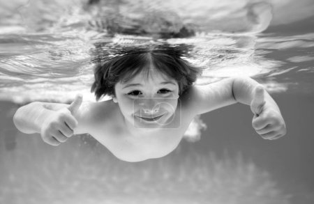 Foto de Cara de niño bajo el agua con los pulgares arriba. Niños bajo el agua nadando en la piscina, niños sanos nadando y divirtiéndose bajo el agua. Juego acuático, actividad deportiva al aire libre saludable para niños - Imagen libre de derechos