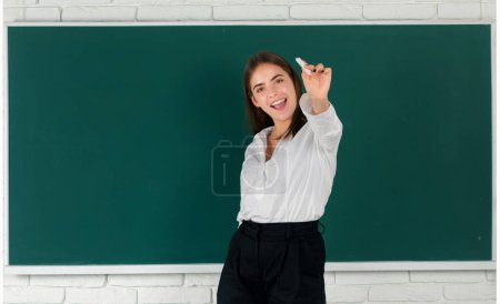 Photo for Excited happy student in university, school education, Young amazed woman holding chalk stand on blackboard background in college classroom - Royalty Free Image