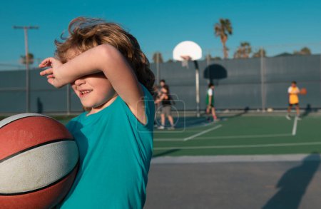 Téléchargez les photos : Fatigué jeune garçon de jouer au basket. Les enfants fatigués ont des émotions sportives. Enfant après avoir joué au basket - en image libre de droit