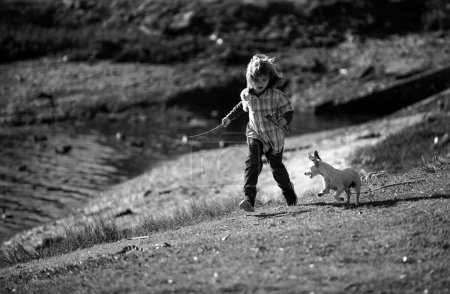 Téléchargez les photos : Enfant et chien drôle courent sur le parc vert. Petit garçon Racing le chiot - en image libre de droit