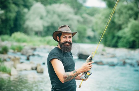 Téléchargez les photos : Fisherman man on river or lake with fishing rod. Hipster bearded man catching trout fish - en image libre de droit