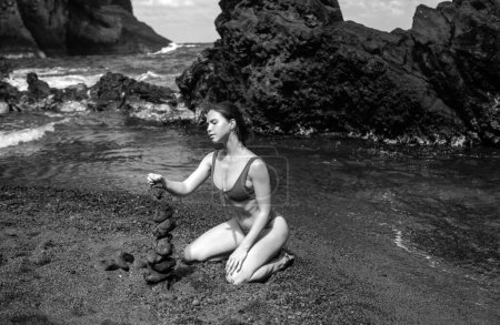 Téléchargez les photos : Jeune femme avec des pierres zen sur la plage de la mer, méditation, spa et harmonie. Calme concept d'équilibre - en image libre de droit