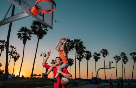 Téléchargez les photos : Basket-ball entraînement garçon enfant avec entraîneur, garçon enfant jetant balle dans le panier de basket-ball à l'extérieur - en image libre de droit