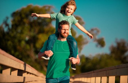 Photo for Father giving son ride on back in park. Portrait of happy father giving son piggyback ride on his shoulders. Cute boy with dad outdoor - Royalty Free Image