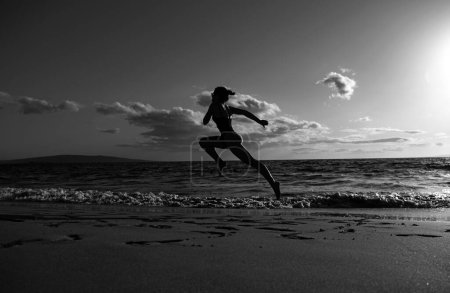 Foto de Mujer corredora en la playa. Mujer corriendo al atardecer en la playa. Deporte de verano y concepto de libertad. Entrenamiento de deportistas en el atardecer - Imagen libre de derechos