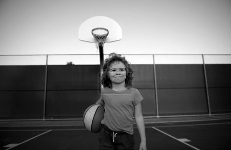 Téléchargez les photos : Petit enfant de sport caucasien jouant au basket tenant le ballon avec le visage heureux - en image libre de droit