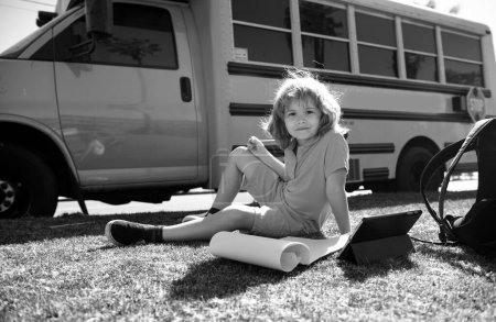 Foto de De vuelta a la escuela. Feliz estudio infantil en el parque cerca del autobús escolar. Colegial haciendo deberes o educación en línea - Imagen libre de derechos