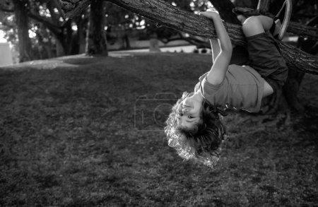 Foto de Niño jugando y trepando a un árbol y colgando boca abajo. Adolescente chico jugando en un parque - Imagen libre de derechos