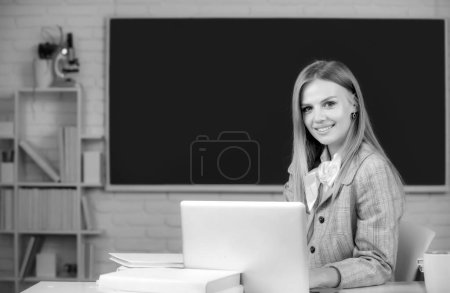 Photo for Portrait of smiling young college student studying, sitting at table and writing on notebook in classroom - Royalty Free Image