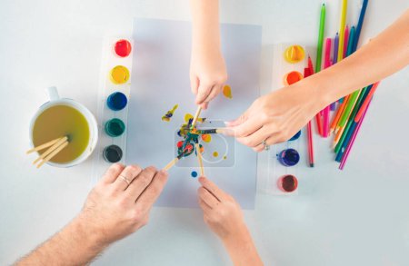Foto de Hands of a family drawing with pencil and paints. Top view to white table with art supplies. Kids learning painting - Imagen libre de derechos