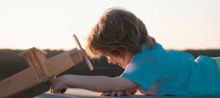 Téléchargez les photos : Enfants jouant avec l'avion en bois vintage à l'extérieur. Portrait d'enfants sur fond de ciel d'été. Concept de voyage et liberté - en image libre de droit