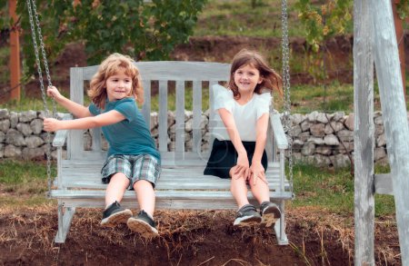 Foto de Dos niños balanceándose y relajándose al aire libre en el parque de verano. Hermano y hermana felices caminando en la naturaleza. Hermanos niño y niña jugando en el jardín - Imagen libre de derechos