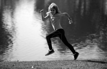 Téléchargez les photos : Enfants courir ou faire du jogging près du lac sur l'herbe dans le parc. Garçons jogging coureur dans le parc extérieur. La course est un sport qui renforce le corps. Jogging matinal - en image libre de droit