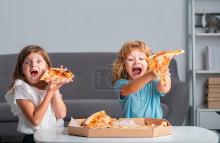 Photo for Children eating pizza. Excited kids eating pizza. Two young children bite pizza indoors - Royalty Free Image