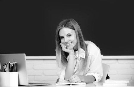 Photo for Smiling student, young cute blonde woman online watching webinar on laptop, listening learning education course, sit at work desk in classroom, elearning concept - Royalty Free Image