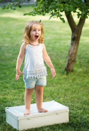 Foto de Niña excitada divirtiéndose en el jardín. Niño en césped de hierba verde durante el paseo en el patio. Feliz infancia y cuidado del bebé - Imagen libre de derechos