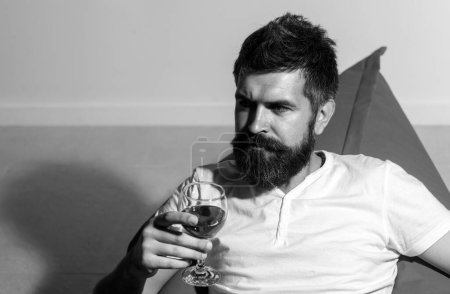 Téléchargez les photos : Hipster barbu avec du vin. À la maison. Homme avec de l'alcool. Homme barbu avec un verre de vin. Mode décontractée - en image libre de droit