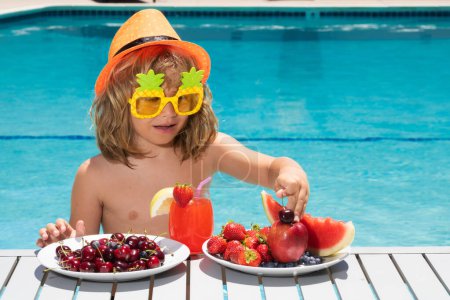 Photo for Healthy food. Outdoor leisure activity with kids by swimming pool. Summertime. Summer child by the pool eating fruit and drinking lemonade cocktail. Summer kids. Little kid boy relaxing in a pool - Royalty Free Image