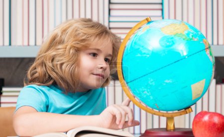 Téléchargez les photos : School kid pupil looking at globe in library at the elementary school. World globe. School kid 7-8 years old with book go back to school. Little student. Education concept - en image libre de droit