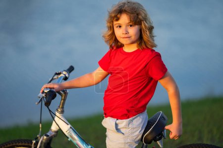 Téléchargez les photos : Petit garçon en vélo dans un parc d'été. Un enfant conduit un vélo sur une allée à l'extérieur. Enfant en vélo dans la ville. Enfant en vélo extérieur. Enfant vélo vélo sur le quartier américain - en image libre de droit