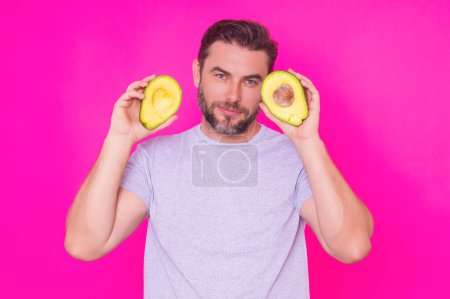 Photo for Man hold half of fresh avocado isolated on pink background, studio portrait. The avocado. Healthy look. Portrait of handsome man hold avocado near his face - Royalty Free Image