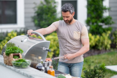 Photo for Cropped image of handsome man is making grill barbecue outdoors on the backyard. Bbq party. Bbq meat, grill for picnic. Roasted on barbecue. Man preparing barbeque in the house yard - Royalty Free Image